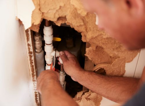 man fixing pipes in exposed wall