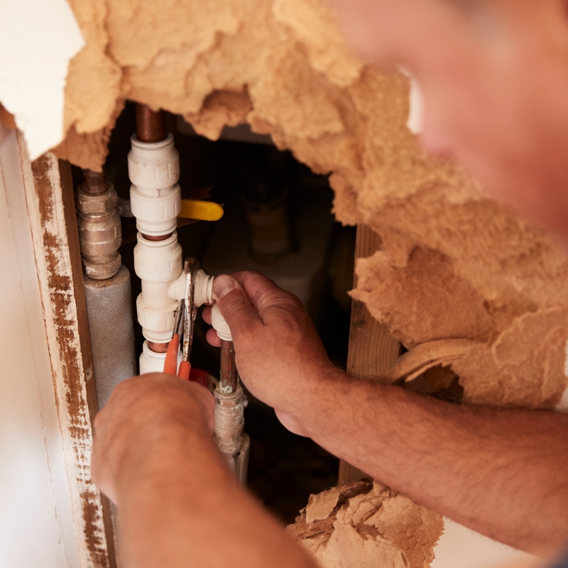 man fixing pipes in exposed wall